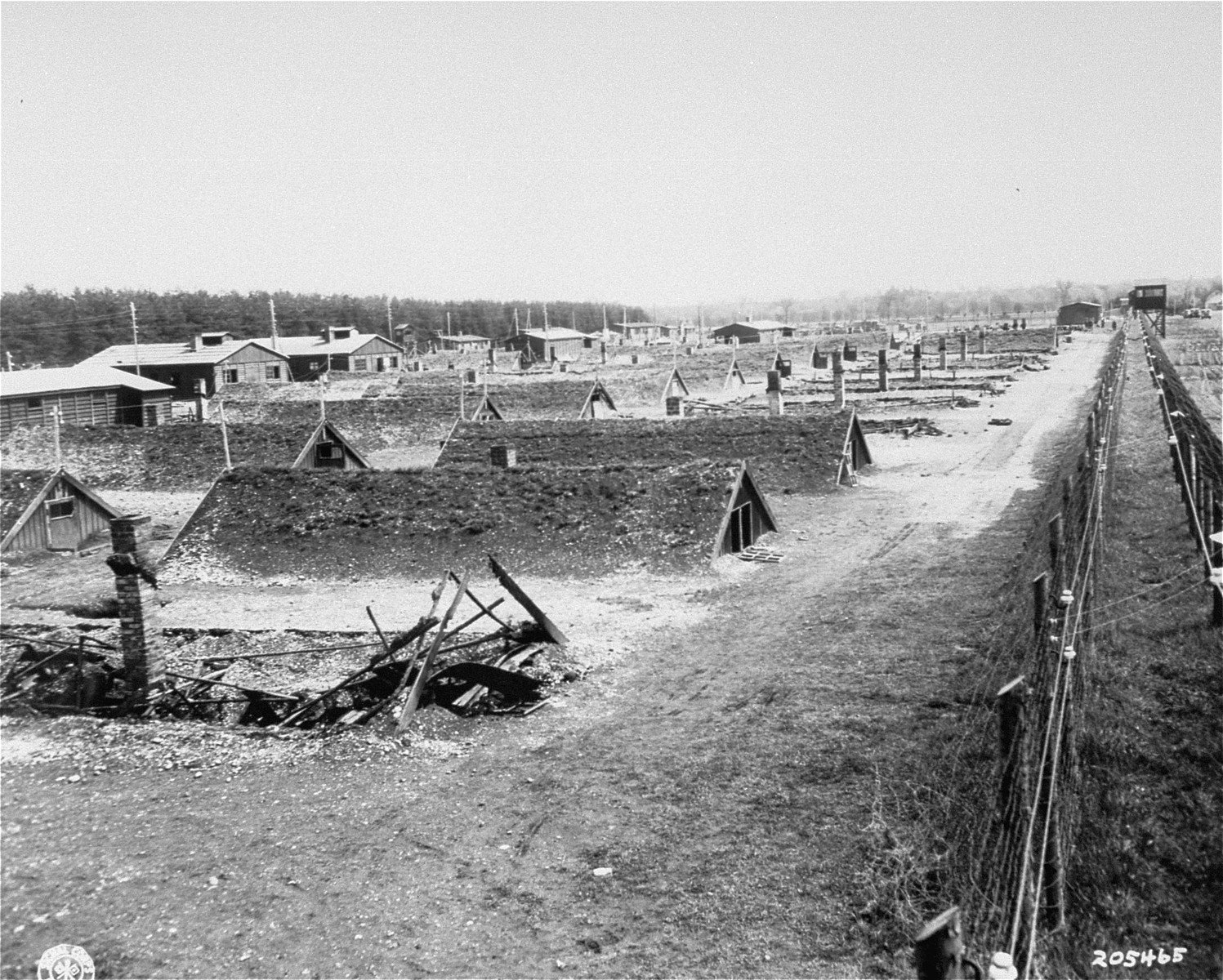 8_KauferingIV_USHMM_TEMP Fotografía antigua, en blanco y negro, de los cuarteles del campo de concentración de Kaufering IV. Las estructuras están construidas parcialmente bajo tierra, de modo que solo los techos en pico están por encima del nivel del suelo; además, están cubiertos con hierba para impedir que se vean desde el aire.