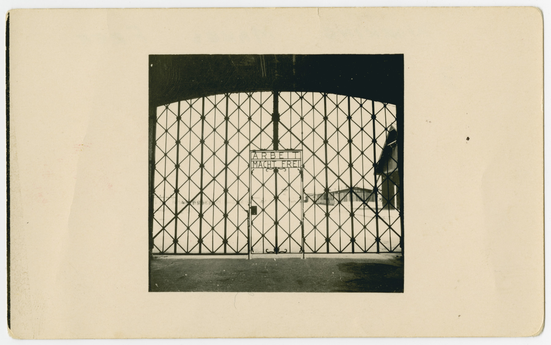 9_DachauGateArbeitMachtFrei_USHMM_TEMP Old, black and white photograph of an iron gate that bears the inscription, "Arbeit Macht Frei" or "Work will set you free."